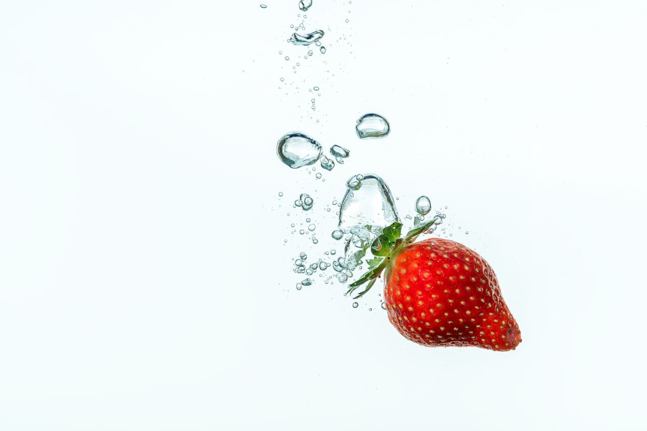 vision Vivid strawberry diving into water with bubbles against white background, showcasing freshness.