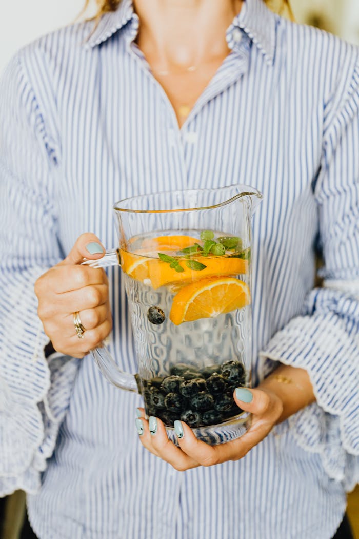 services-03 A close-up of a person holding a pitcher of refreshing citrus and berry infused water with mint leaves.