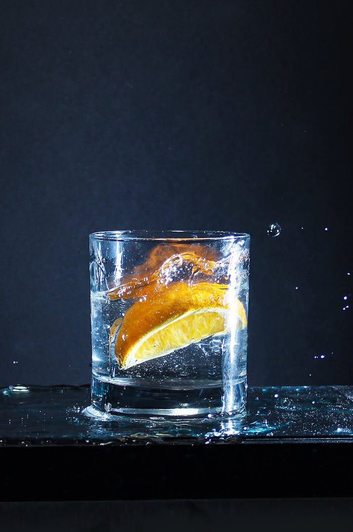 A glass of water with a lemon slice splashing, captured against a dark background.